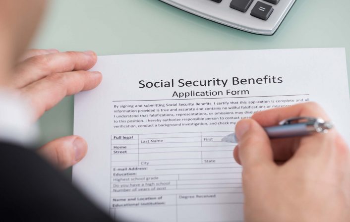 Close-up Of Person Hand Filling Social Security Benefits Form